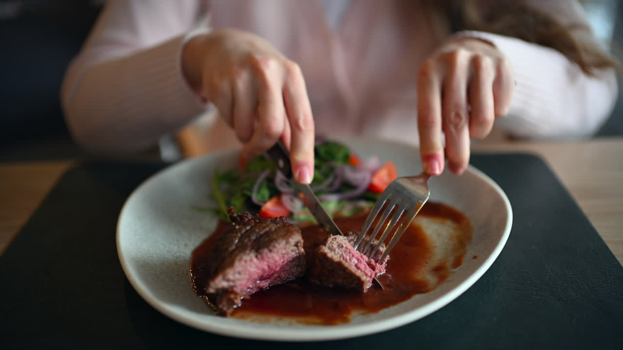 Close up of woman cutting juicy grilled steak served with rich sauce and fresh salad