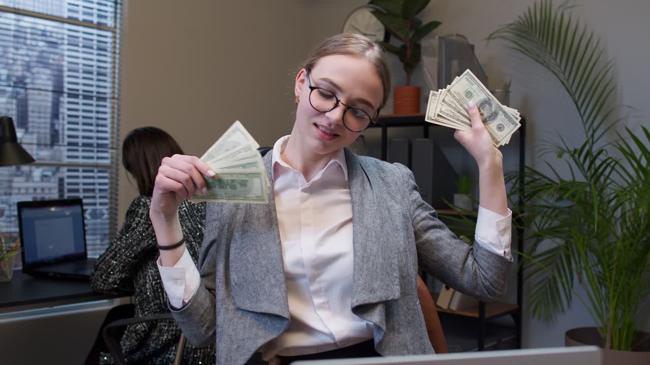 Businesswoman company manager celebrating success, dancing with stack of money dollar cash in office