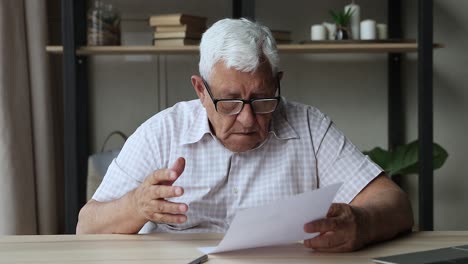 stressed aged man troubled with bad news from paper letter