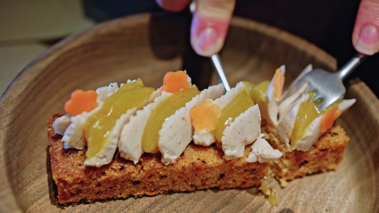 Close up of a slice of moist carrot cake topped with cream cheese frosting or soft cream slices, drizzled with a yellow fruit sauce