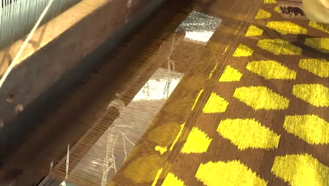 close-up of hands weaving vibrant yellow patterns on a traditional loom, showcasing intricate craftsmanship.