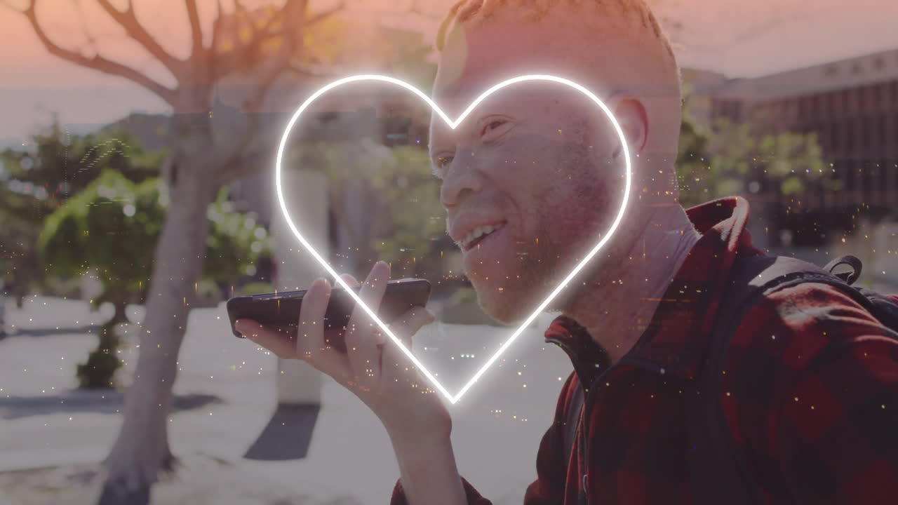Man speaking into smartphone in urban plaza, showcasing neon heart overlay graphic in tech demo