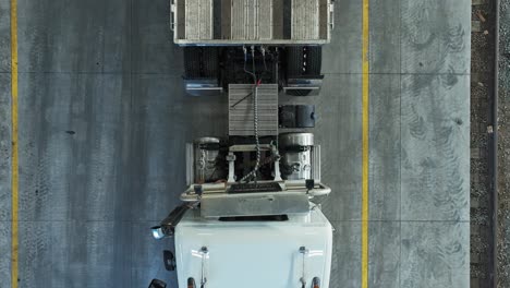 drone top down tracking pan across semi truck and empty trailer in warehouse