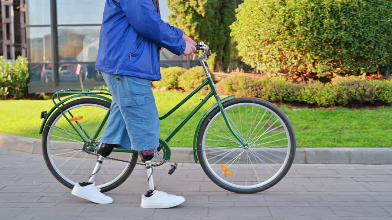 View of a man with prosthetic legs. Walking with a bicycle on the street with greenery