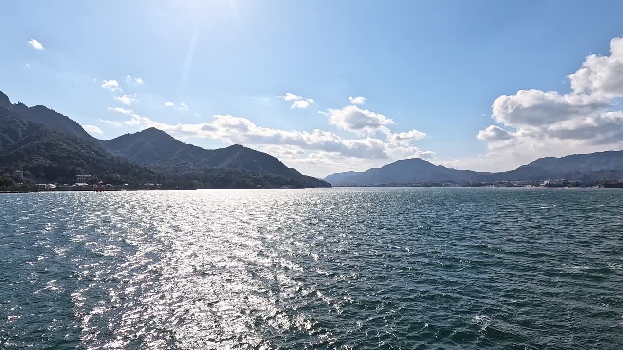 Sunlit ferry deck with wooden benches overlooking Hiroshima Bay near Miyajima, Japan. Opening shot revealing the entire sea view