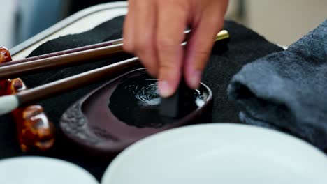 footage of a japanese man painting a nihonga, a traditional japanese painting, with brushes and black ink
