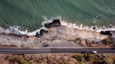 Aerial:-Birds-eye-view-looking-down-as-cars-drive-along-the-Captain-Cook-Highway-next-to-the-ocean,-between-Cairns-and-Port-Douglas,-Far-North-Queensland