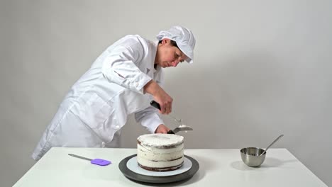 fotografía frontal de un panadero usando una espátula de helado para tocar cuidadosamente los lados del pastel cubierto de crema.