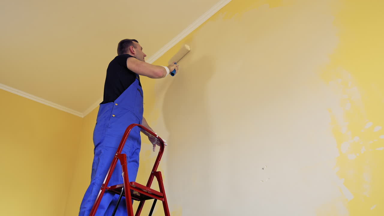 Man painting a yellow wall with a roller at work. Offering professional painting services.