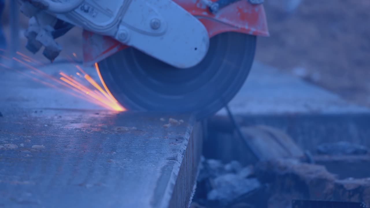 строитель с помощью мельницы отрезает часть толстой плиты, много искр и дыма