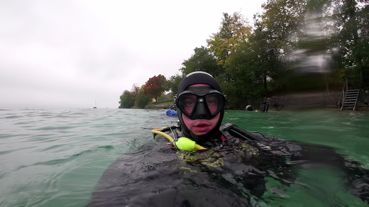 Scuba divers in a large freshwater lake float on the surface