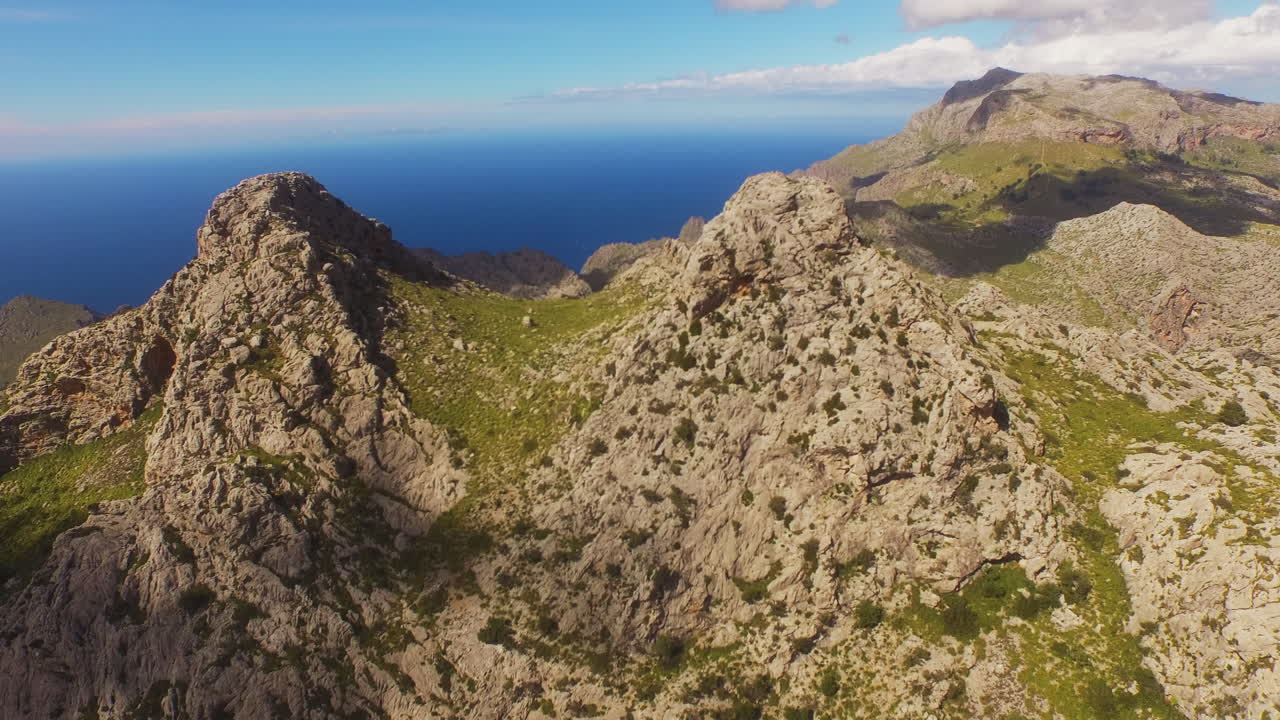 Vista aerea discendente sulle montagne rocciose con ombre di nuvole e il mare visibile in lontananza a Maiorca