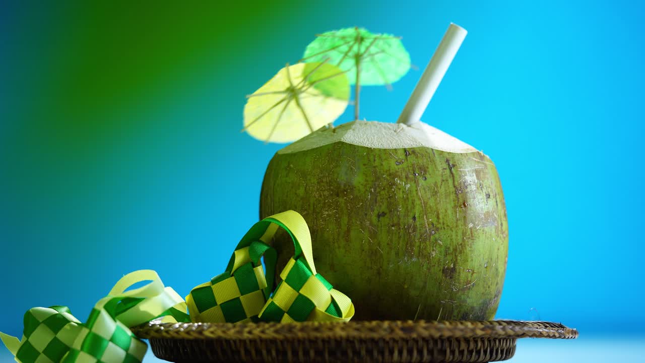 bebida tropical de coco con mini paraguas como decoración y cinta ketupat contra fondo azul