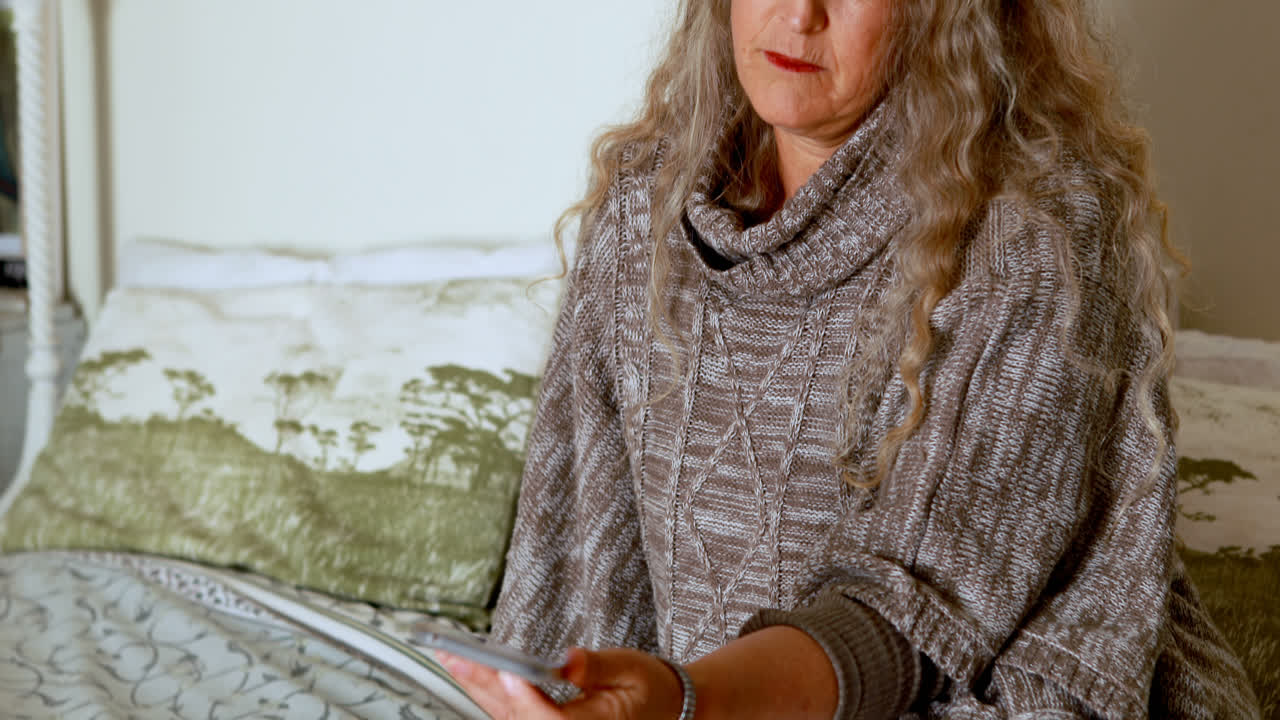 зрелая женщина использует мобильный телефон в спальне 4k