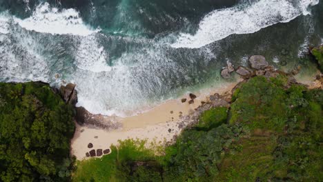 overhead drone shot of white sandy beach between cliffs - tropical beach of indonesia