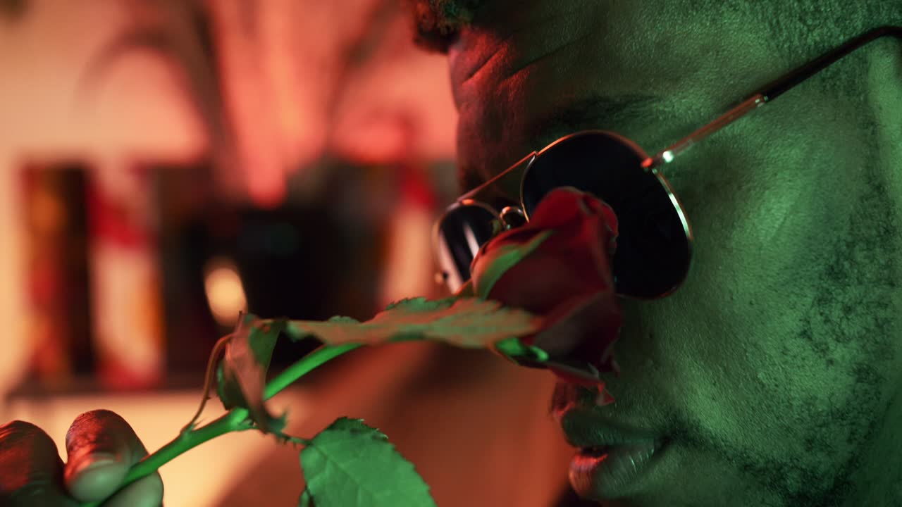 chico negro en una habitación de luz verde con una hermosa rosa roja tocando su cara - cerrar