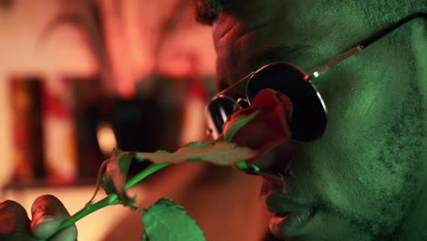 Black-Guy-In-Green-Light-Room-With-Beautiful-Red-Rose-Touching-His-Face---close-up