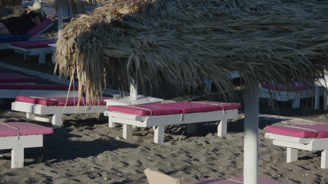 Panorama of multiple relaxing lounge chairs on volcanic black sand at beach club near ocean in Santorini, Greece