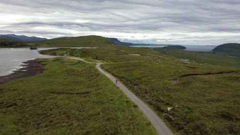 male on a longboard zigzagging over a gray asphalt road between the beautiful green nature in the scottish wilderness on a cloudy day