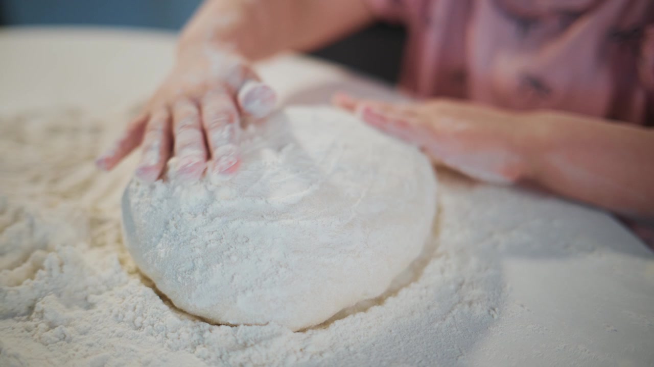 Child kneads dough on floured surface. Hands covered in flour, focused and concentrated. Satisfying, tactile moment of baking preparation. Ideal for recipes, cooking tutorials, family kitchen scenes