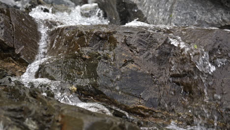 zoom in shot of water falling between rocks in a waterfall, close up view in slow motion