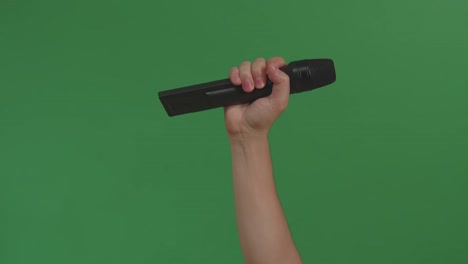male hand holding microphone against background green screen chroma key. close up mic, live press conference, karaoke, singer performance