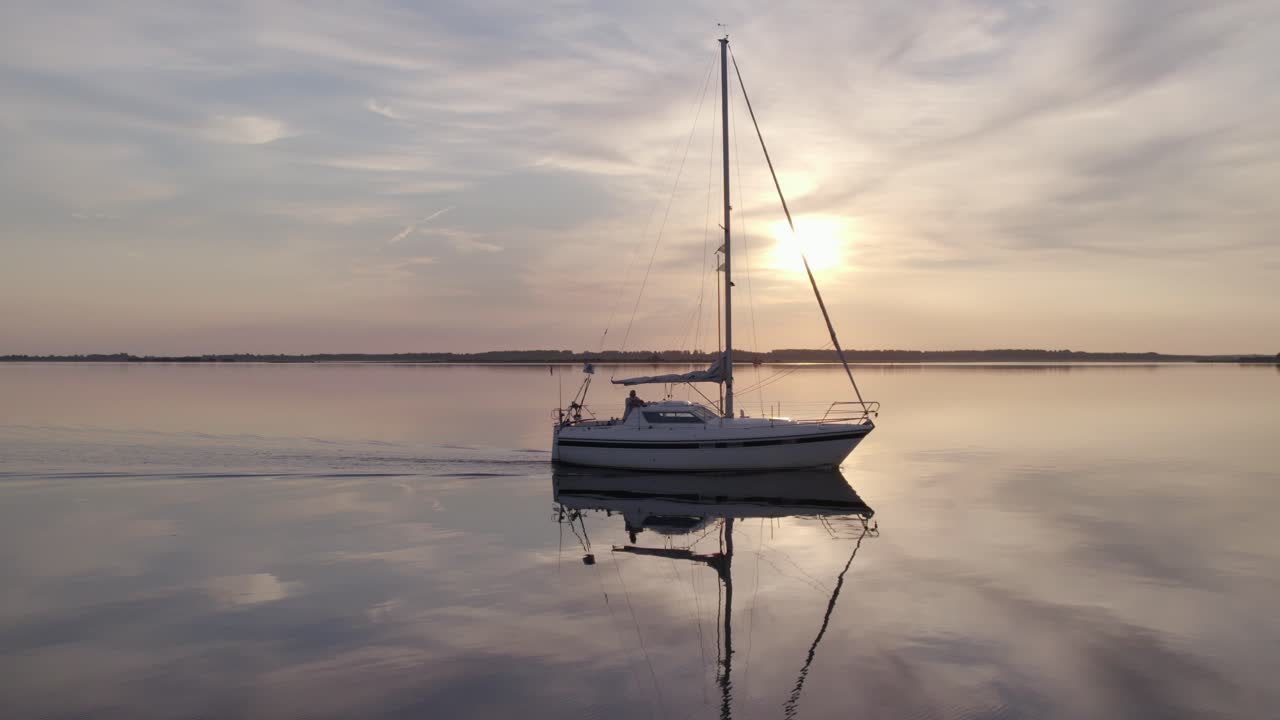 Vista aerea di uno yacht a vela e riflessi sul lago all'alba a Lauwersoog, Paesi Bassi, con una splendida illuminazione all'alba o al tramonto, atmosfera calma, riprese drone di alta qualità che rivelano uno scenario pacifico