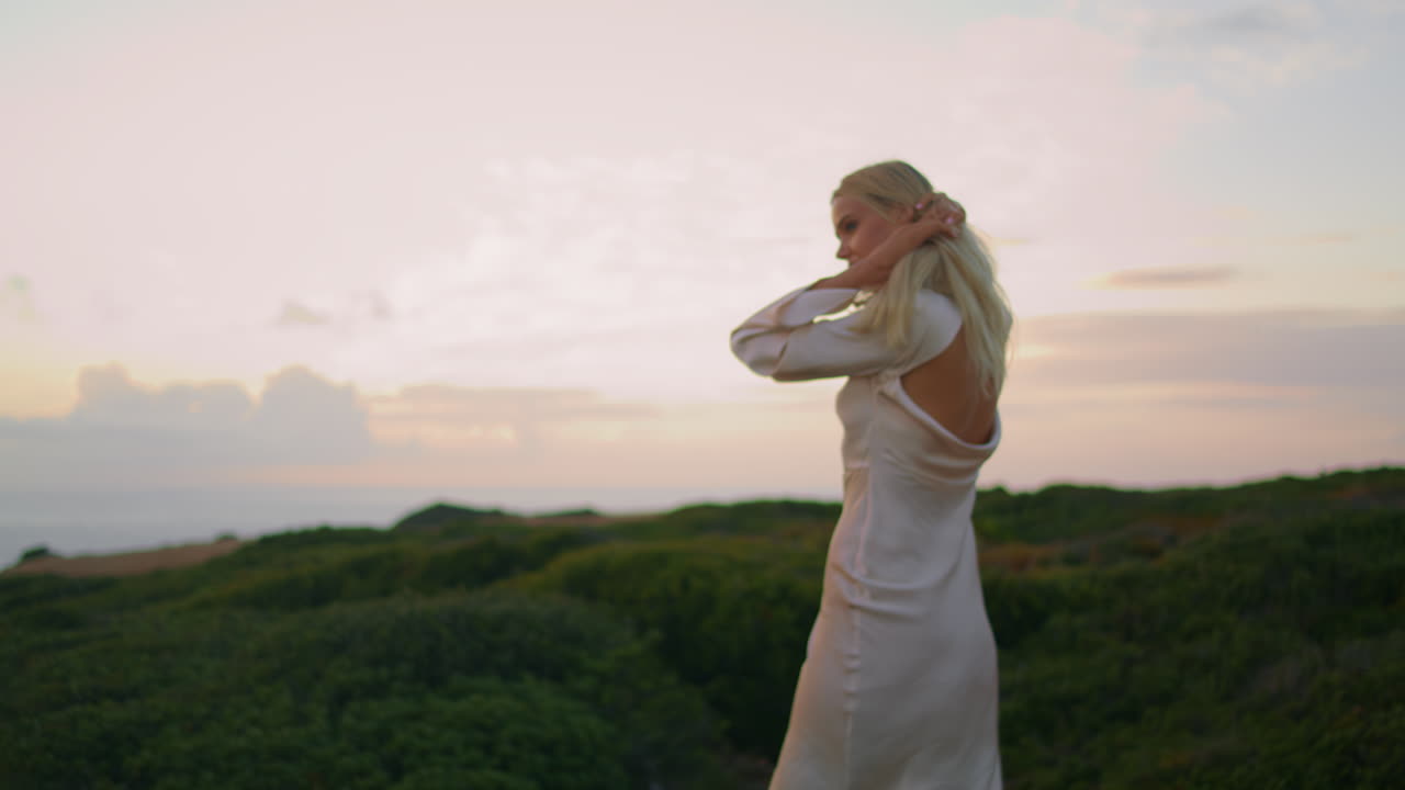 평온한 자연의 클로즈업에서 웃는 힐스 모델. 해가 지는 해안을 포즈하는 소녀