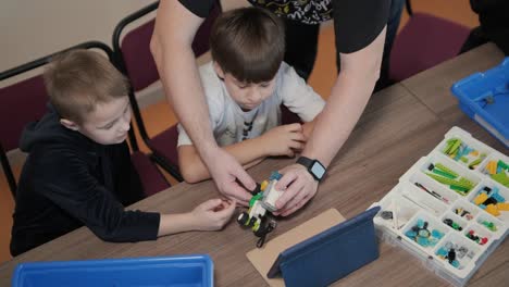 children intently focused on assembling parts from a robotics kit, with a tablet displaying instructions, promoting stem learning and creativity