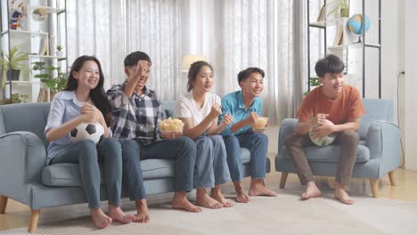 asian teenagers cheering and watching football game on tv and celebrating victory at home