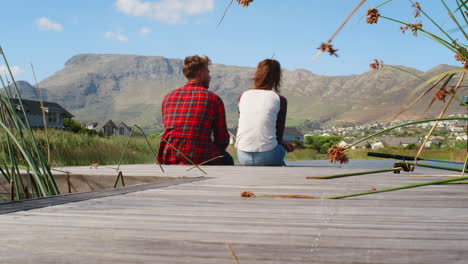 couple sitting on a jetty by a lake and mountains, back view