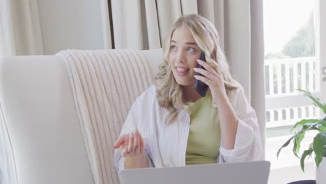 mujer caucásica feliz de talla grande hablando en un teléfono inteligente y usando una computadora portátil en cámara lenta