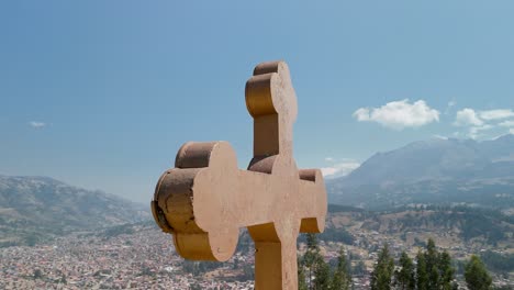 a stunning aerial parallax shot orbits the large cross at the rataquenua viewpoint, revealing a panoramic view of the city of huaraz nestled in a valley in the peruvian andes