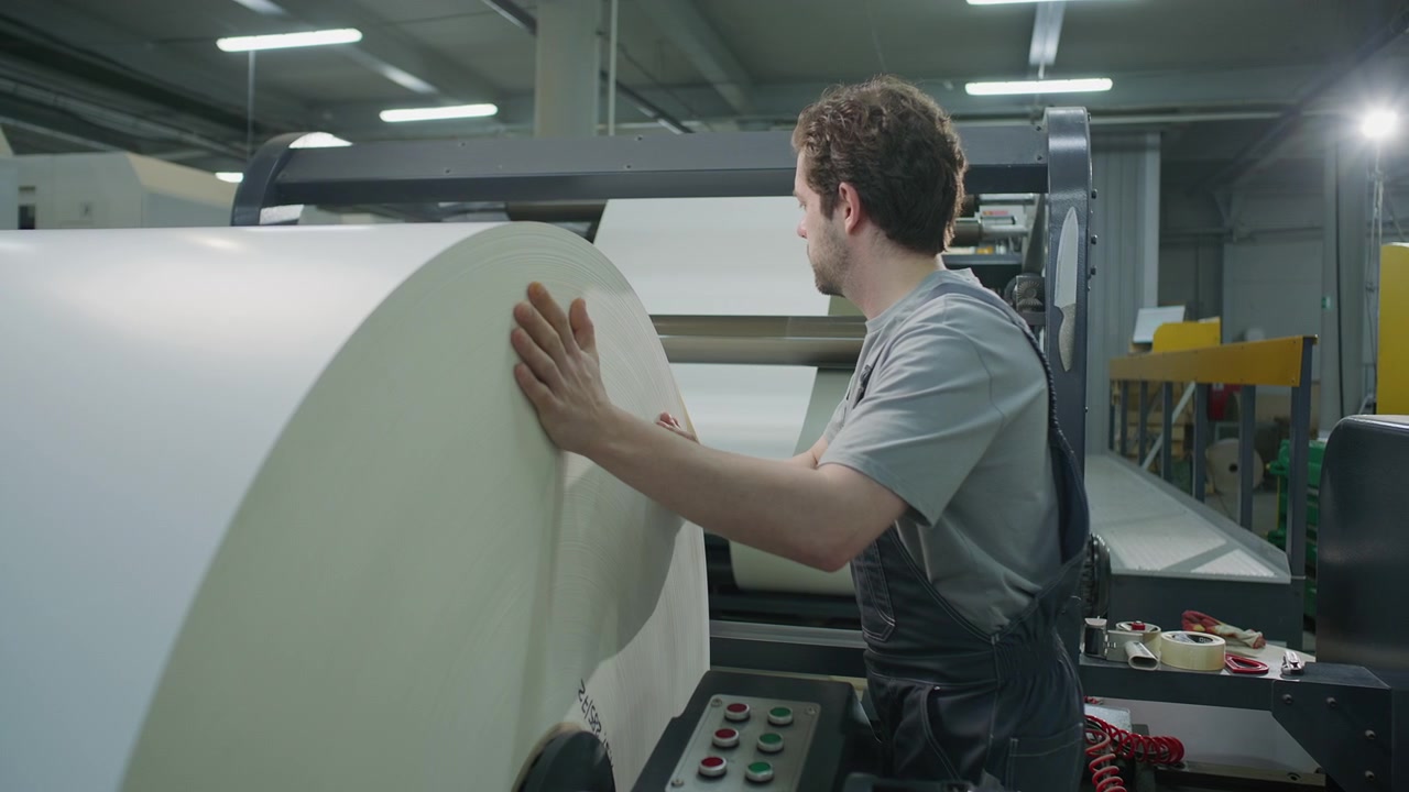 Technician Loading Massive Paper Roll onto Web Press in Printing Factory