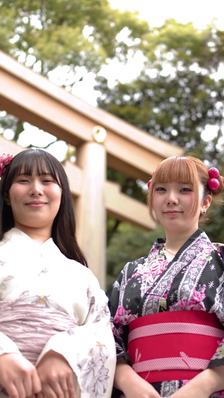 Tokyo'da, geleneksel kimono giymiş iki kadın ahşap bir torii kapısının önünde gülümseyerek duruyor.
