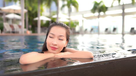 close up of an attractive woman resting her chin on her arms while leaning on the edge of a resort swimming pool