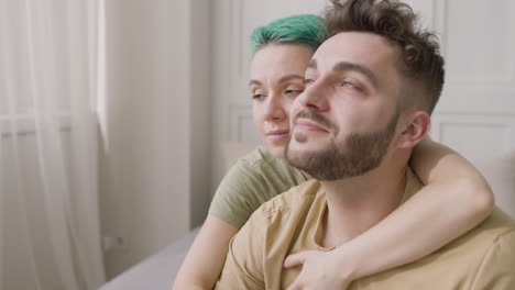 hombre guapo sentado en la cama mientras su novia lo abraza por la espalda