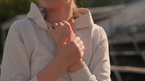 close-up of woman crossing her hands over her hoodie collar, gently touching her neck in a reflective, serene moment, sunlight softly illuminates her skin