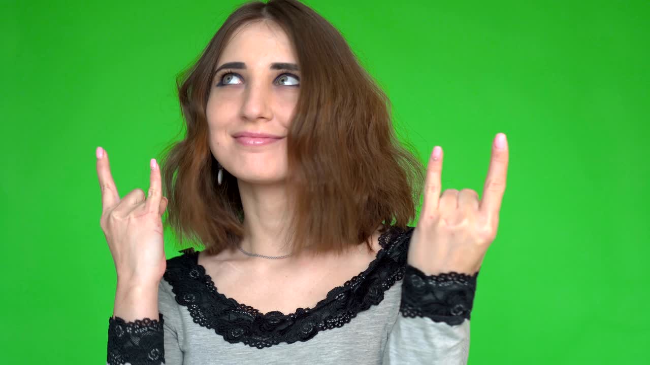 Punk is not dead. Attractive cool young woman making horn sign hand gesture over green background