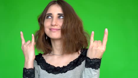 punk is not dead. attractive cool young woman making horn sign hand gesture over green background