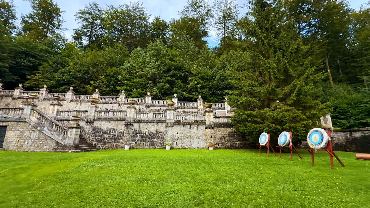 Green lawn and terraced brick stairs near the castle. Three archery targets are on the grass. The Cantacuzino Castle, Bu?teni, Romania