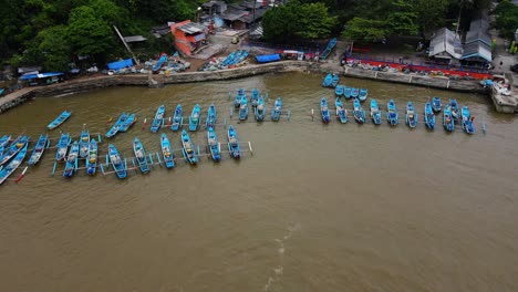 Orbit-drone-shot-of-fishermen-boats-anchored-on-the-harbour-with-market-buildings-and-fish-auctions---Baron-Beach,-Yogyakarta,-Indonesia