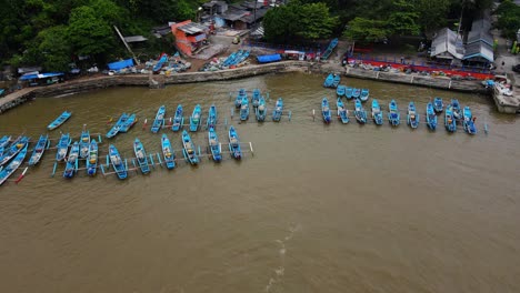 orbit drone shot of fishermen boats anchored on the harbour with market buildings and fish auctions - baron beach, yogyakarta, indonesia