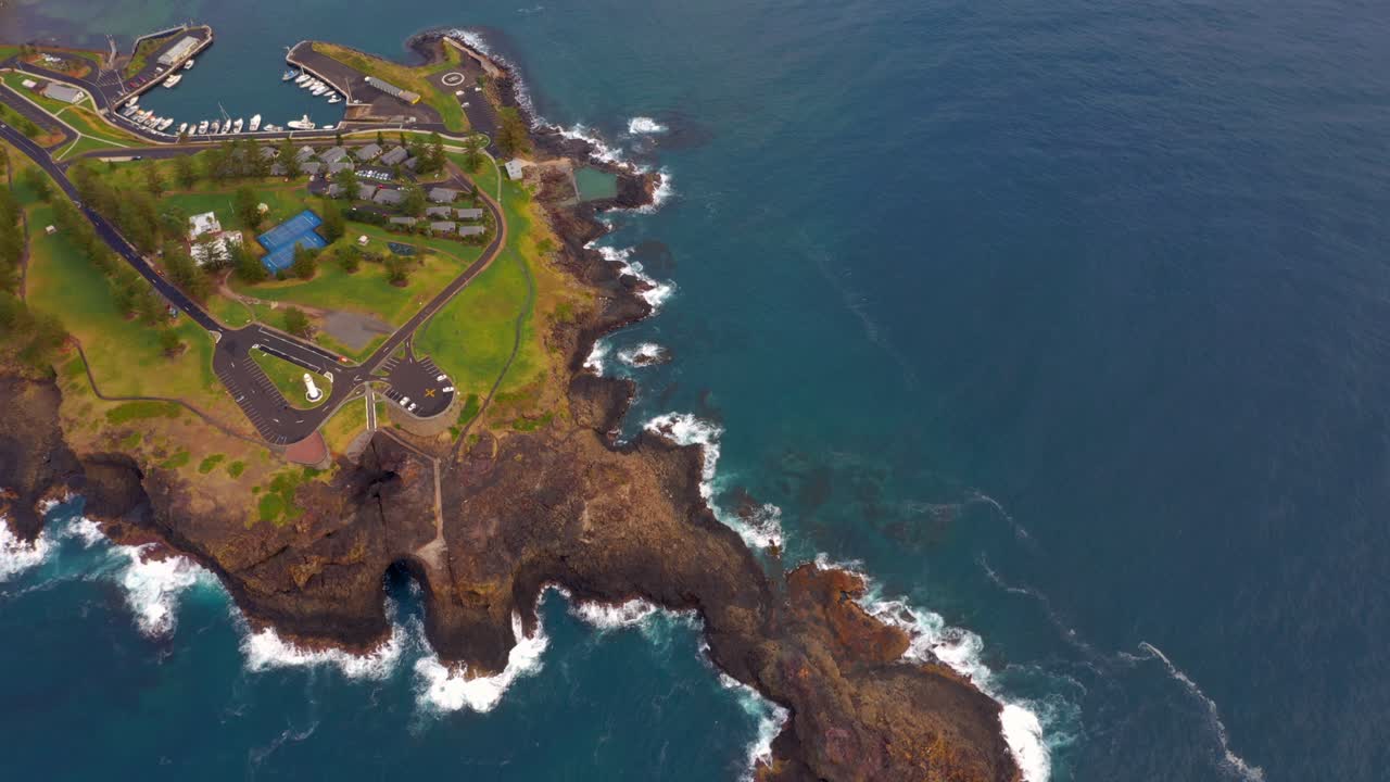 vista de arriba hacia abajo del promontorio de arenisca con faro blanco y muro de piedra de rompeolas que protege el puerto y el puerto deportivo de wollongong en nsw, australia - toma aérea