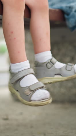 un primer plano de las piernas de dos niños pequeños mientras balancean casualmente sus pies hacia adelante y hacia atrás, una pierna está cruzada, y una bicicleta verde está estacionada cerca