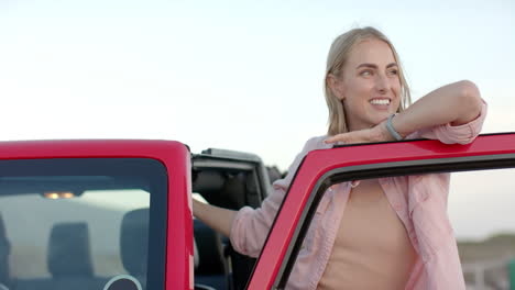 young caucasian woman leans on a red car door on a road trip, with copy space