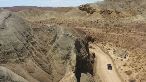 Schwarzer-Suv-Fährt-Schnell-Eine-Unbefestigte-Straße-Im-Regenbogenbecken-In-Der-Mojave-wüste-Hinunter