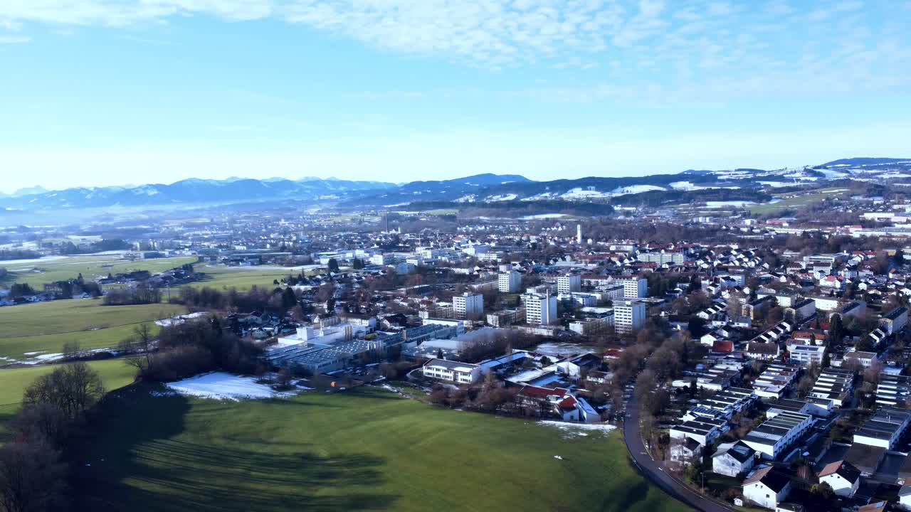 Peaceful city in southern Germany with chaotically laid out houses in the foreground, snow-covered hills revealed after the drone pans to the side