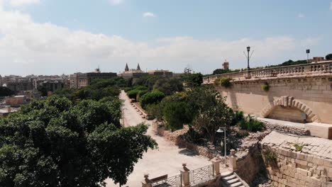 Scenic-aerial-drone-view-of-Herbert-Ganado-garden-and-park-near-Valletta-and-Floriana-city-in-the-background,-Malta