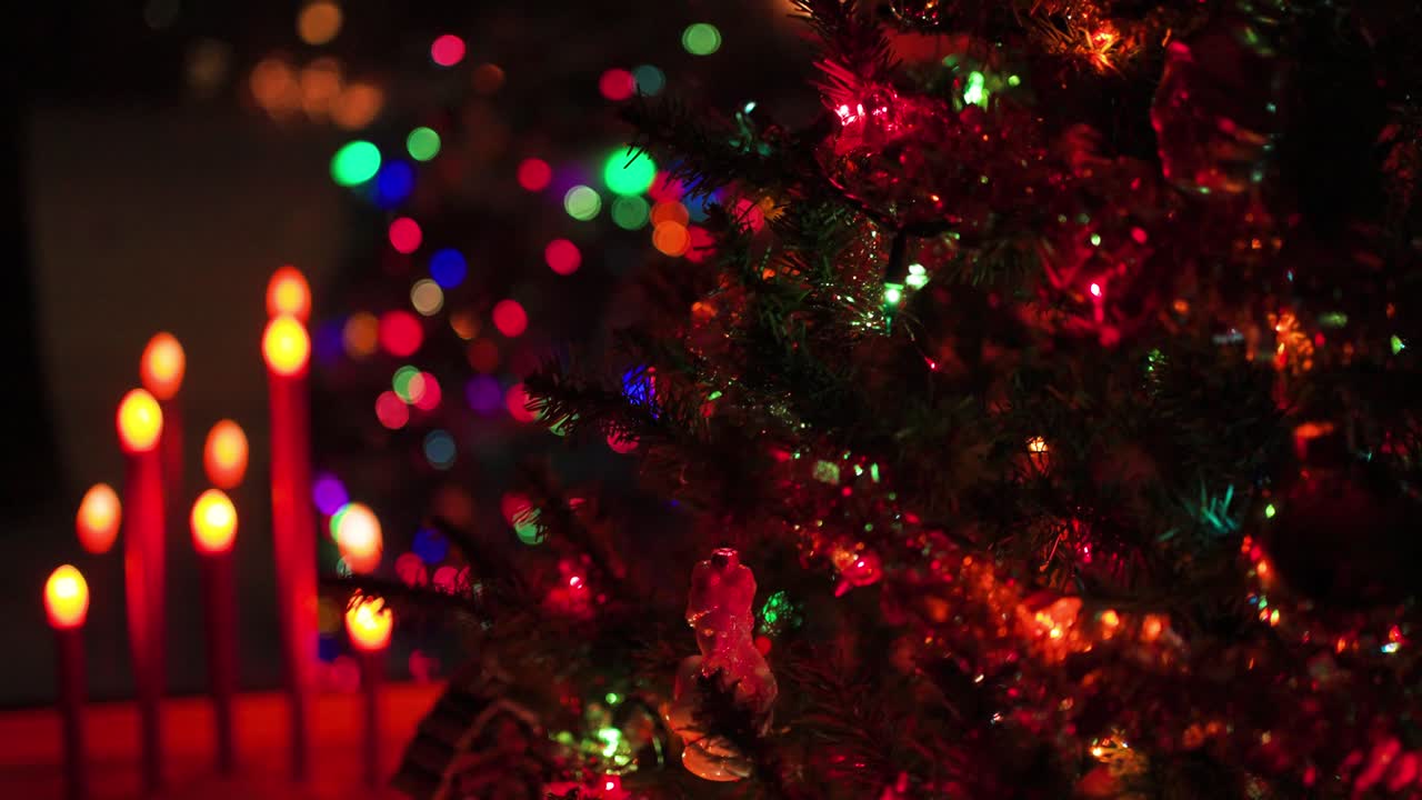 Christmas Tree at night with lights, ornaments and candles in background.